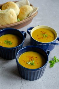 Moroccan red lentil soup served in blue soup bowls. Fresh parsley and sweet paprika as a garnish on the top. Vegan dinner rolls in the background