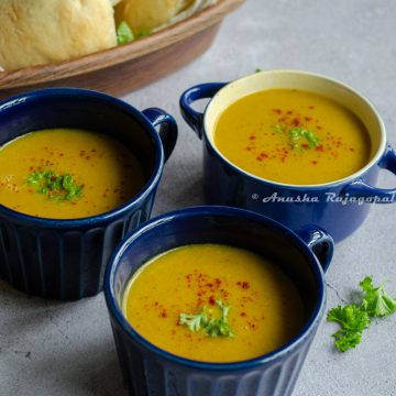 Moroccan red lentil soup served in blue soup bowls. Fresh parsley and sweet paprika as a garnish on the top. Vegan dinner rolls in the background