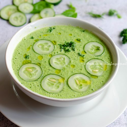 cucumber gazpacho topped with cucumber slices and herbs served in a white bowl set against a white background