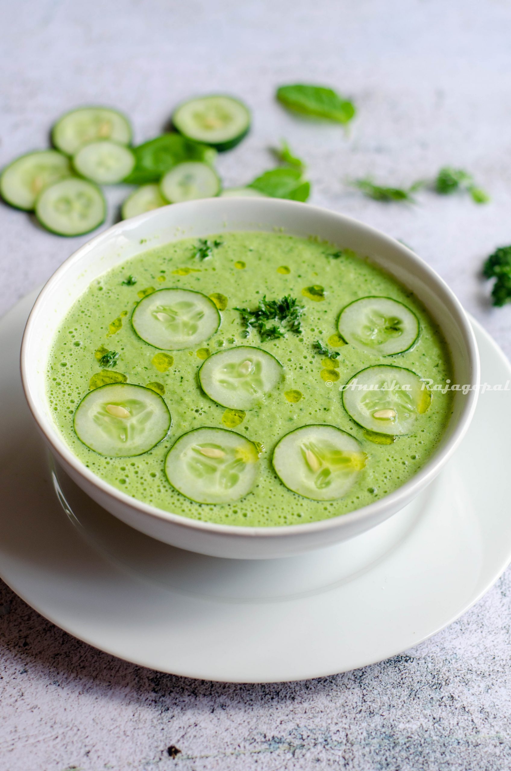 cucumber gazpacho topped with cucumber slices and herbs served in a white bowl set against a white background