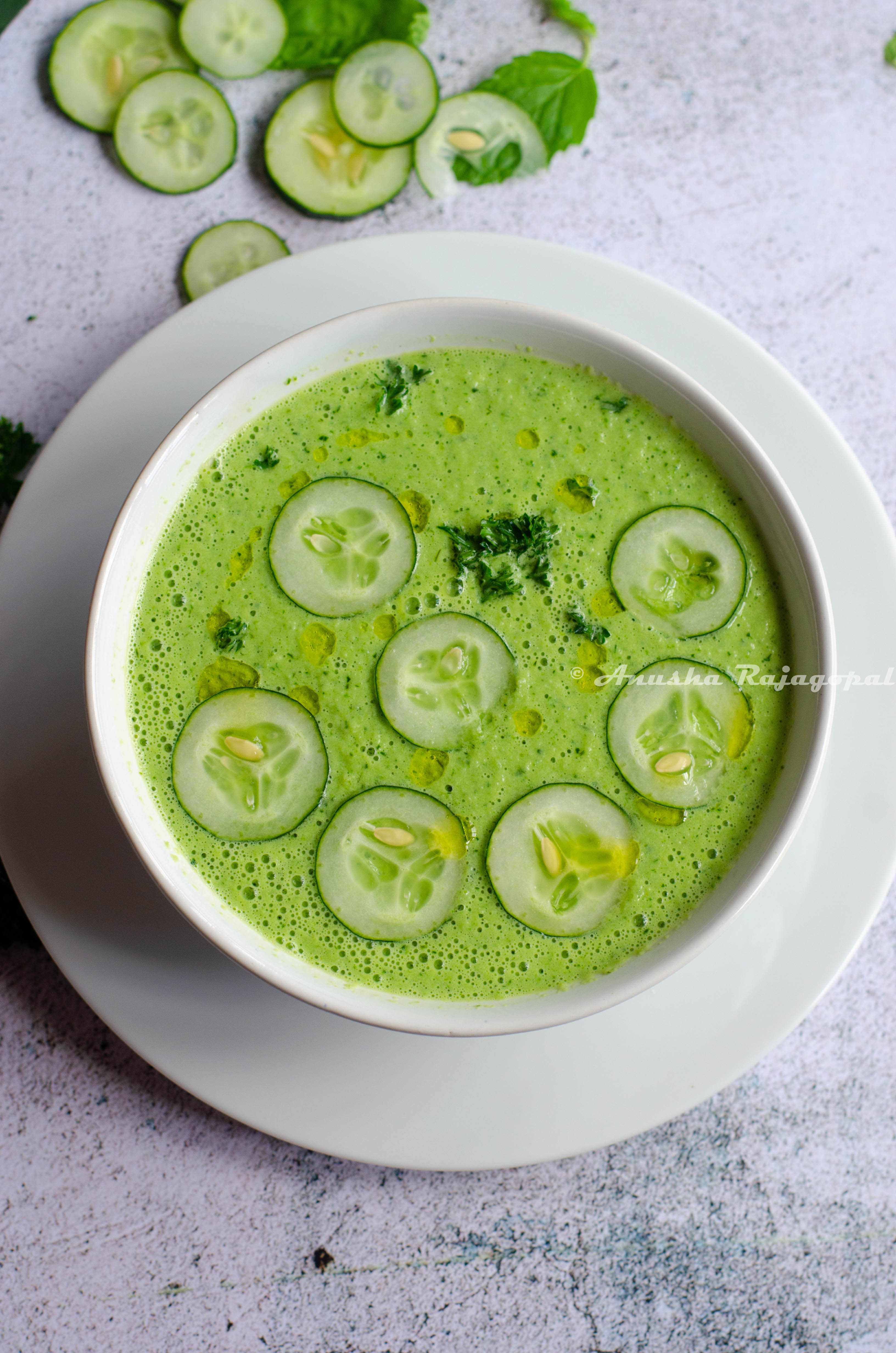 cucumber gazpacho topped with cucumber slices and herbs served in a white bowl set against a white background