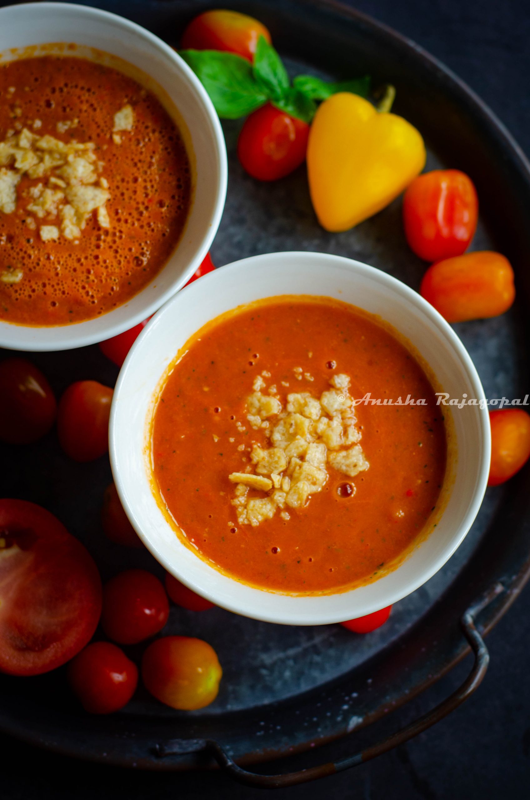 raw vegan tomato gazpacho served in soup bowls with sweet peppers scattered at the background