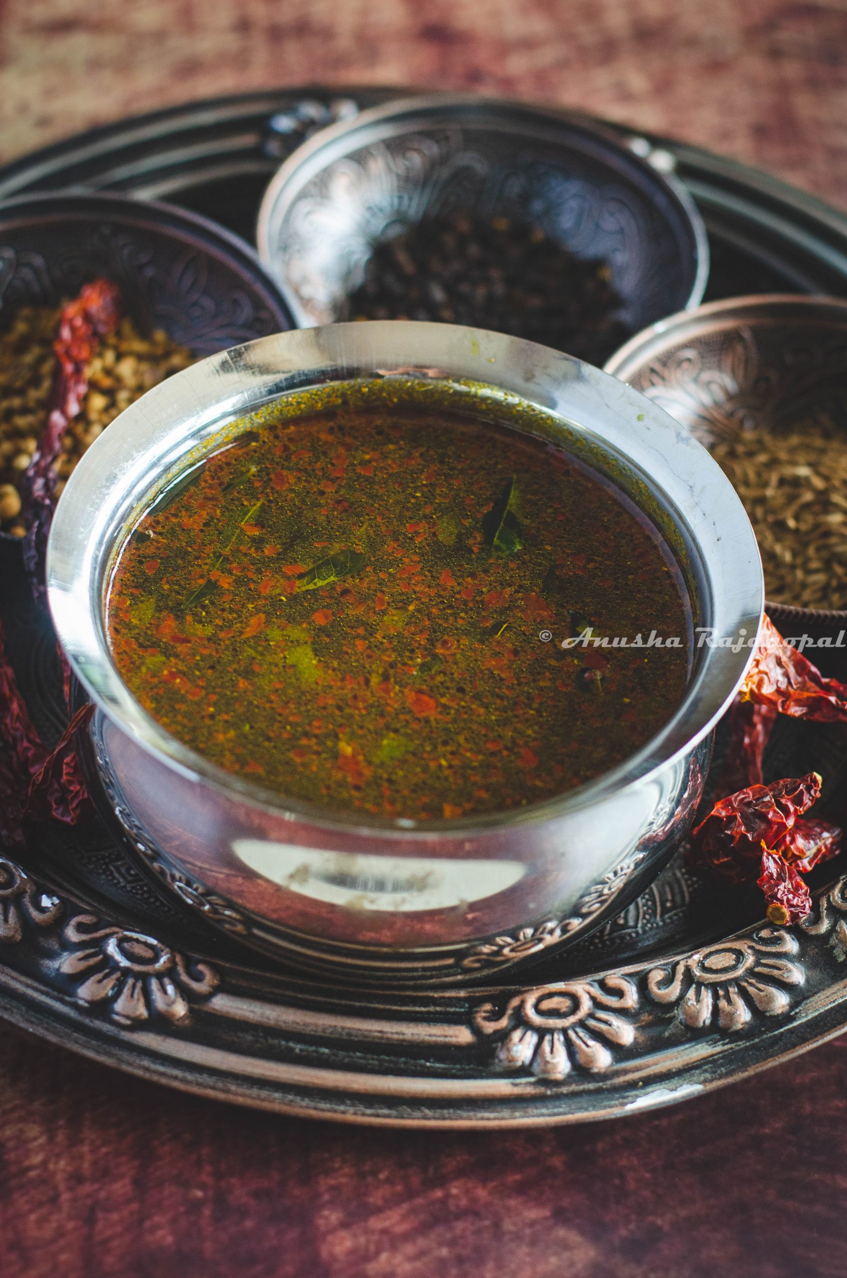 Jeeraga Rasam served in a stainless steel bowl on a vintage tray with spices at the background