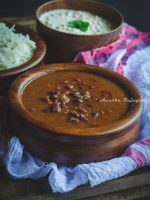 Rajma Masala served in a wooden bowl placed over a white cheese cloth. Jeera rice and a chilled raita topped with mint leaves at the background