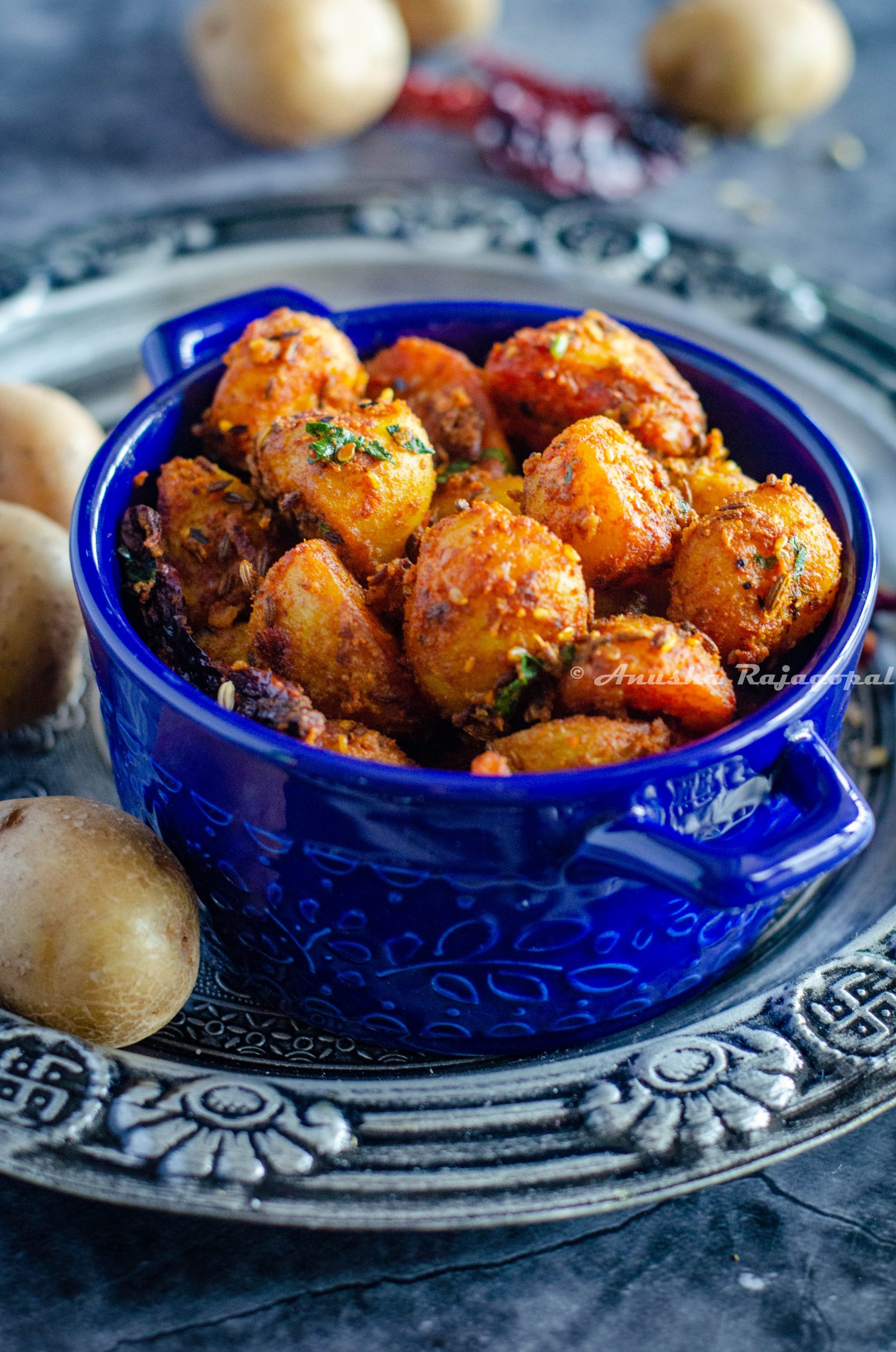 Jodhpuri aloo served in a blue casserole bowl placed over a silver plate