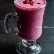 vegan berry rose lassi served in a tall glass placed on a black table