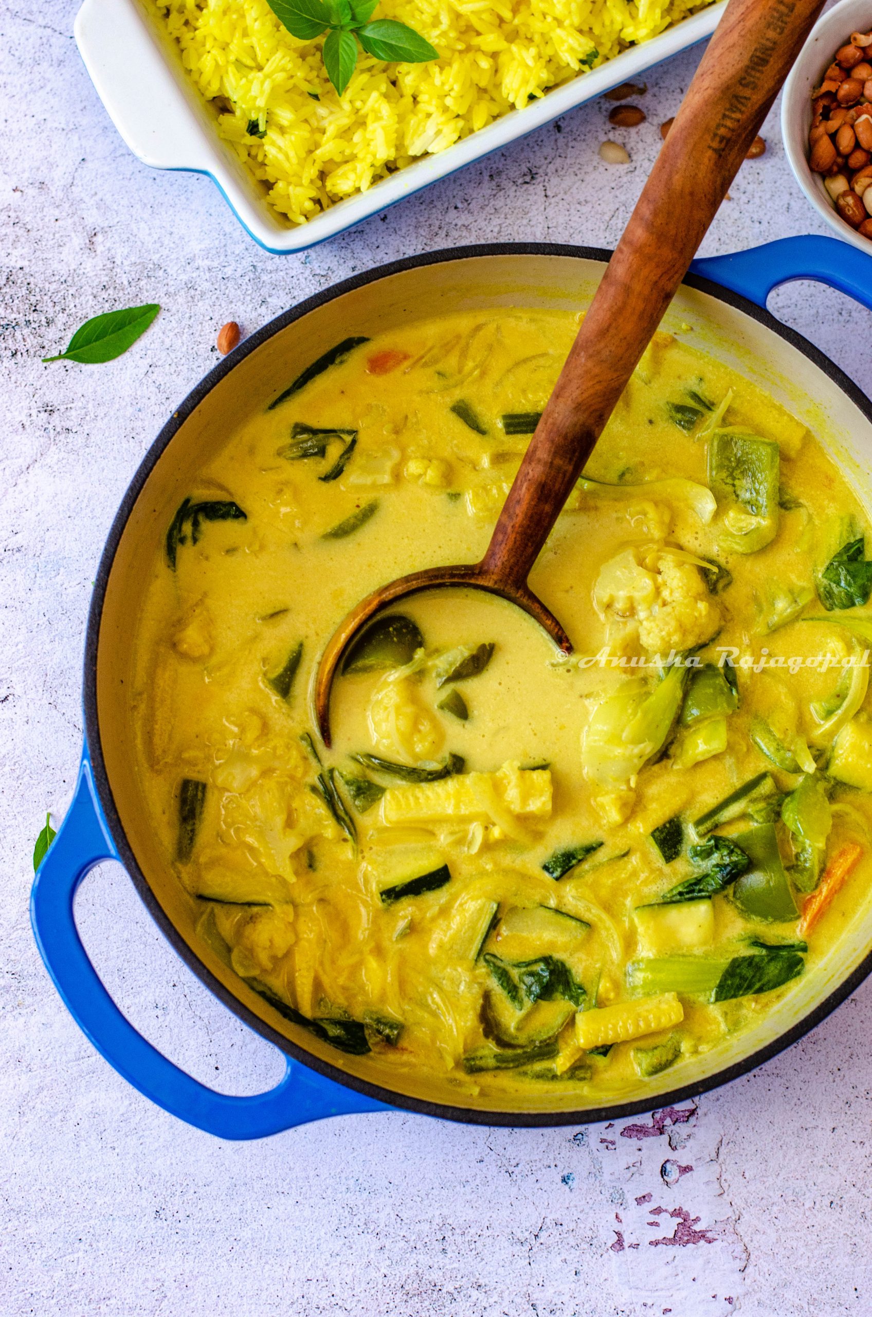 vegan thai yellow curry served in a pan with a wooden ladle
