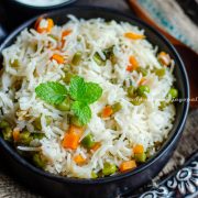 instant pot vegetable pulao in a black bowl served with cucumber raita. both bowls placed on a burlap mat over a rustic platter.