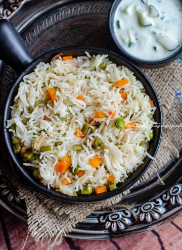 instant pot vegetable pulao in a black bowl served with cucumber raita. both bowls placed on a burlap mat over a rustic platter.