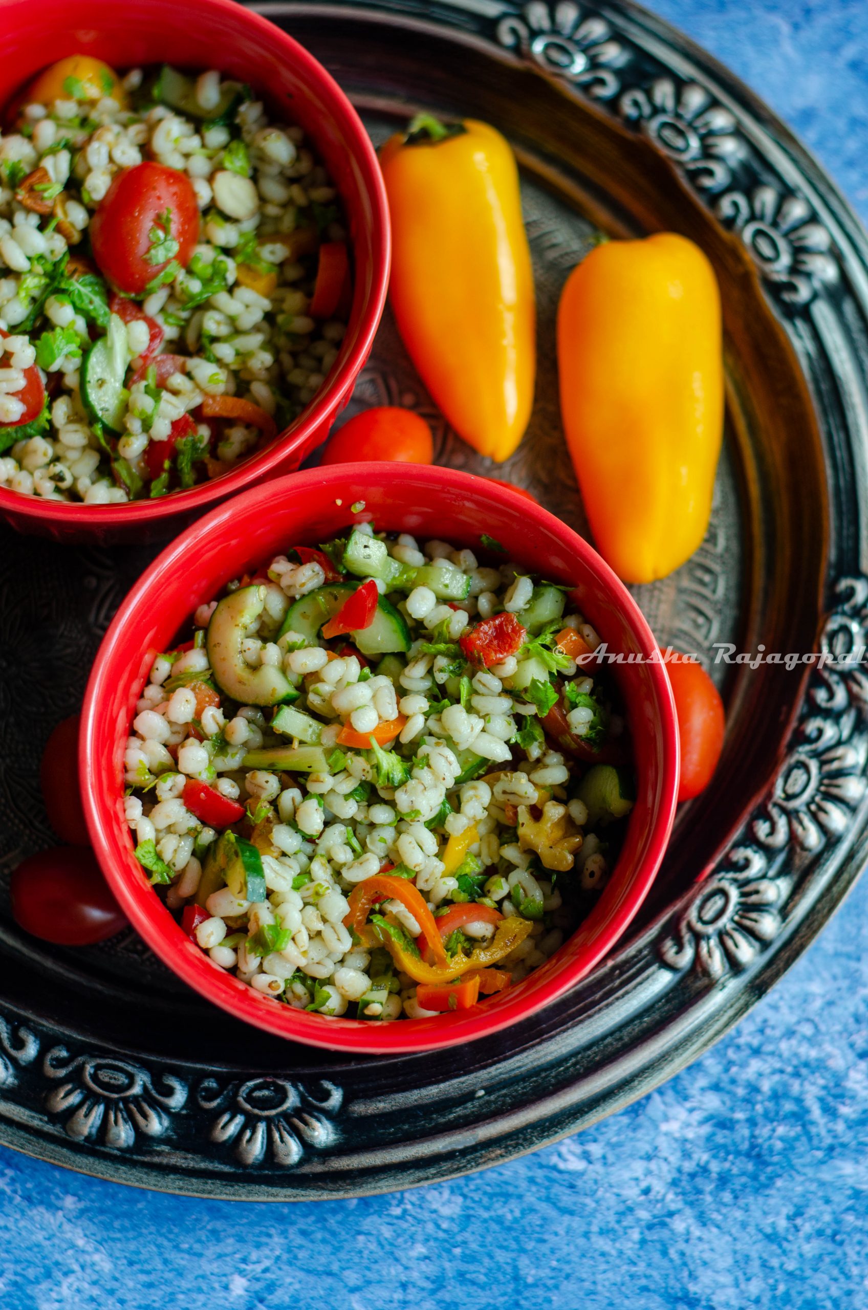 pearl barley tabbouleh salad served in two red bowls placed on a grey rustic platter.
