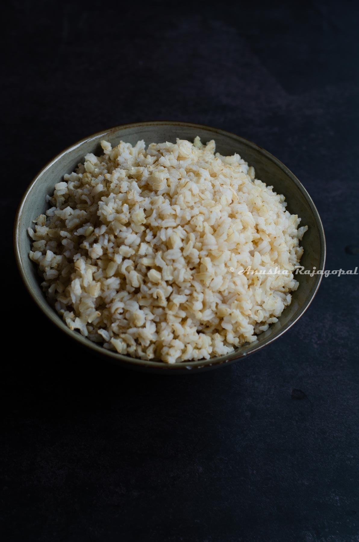 brown sona masoori rice cooked in instant pot served in a grey bowl set against a black background