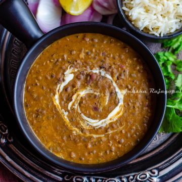 instant pot vegan dal makhani served in a black ladled bowl placed on an antique plate. Lemon wedges and onions with cumin rice by the side.