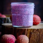 lychee rose chia pudding in a glass jar perched on a wooden tray, lychees scattered around