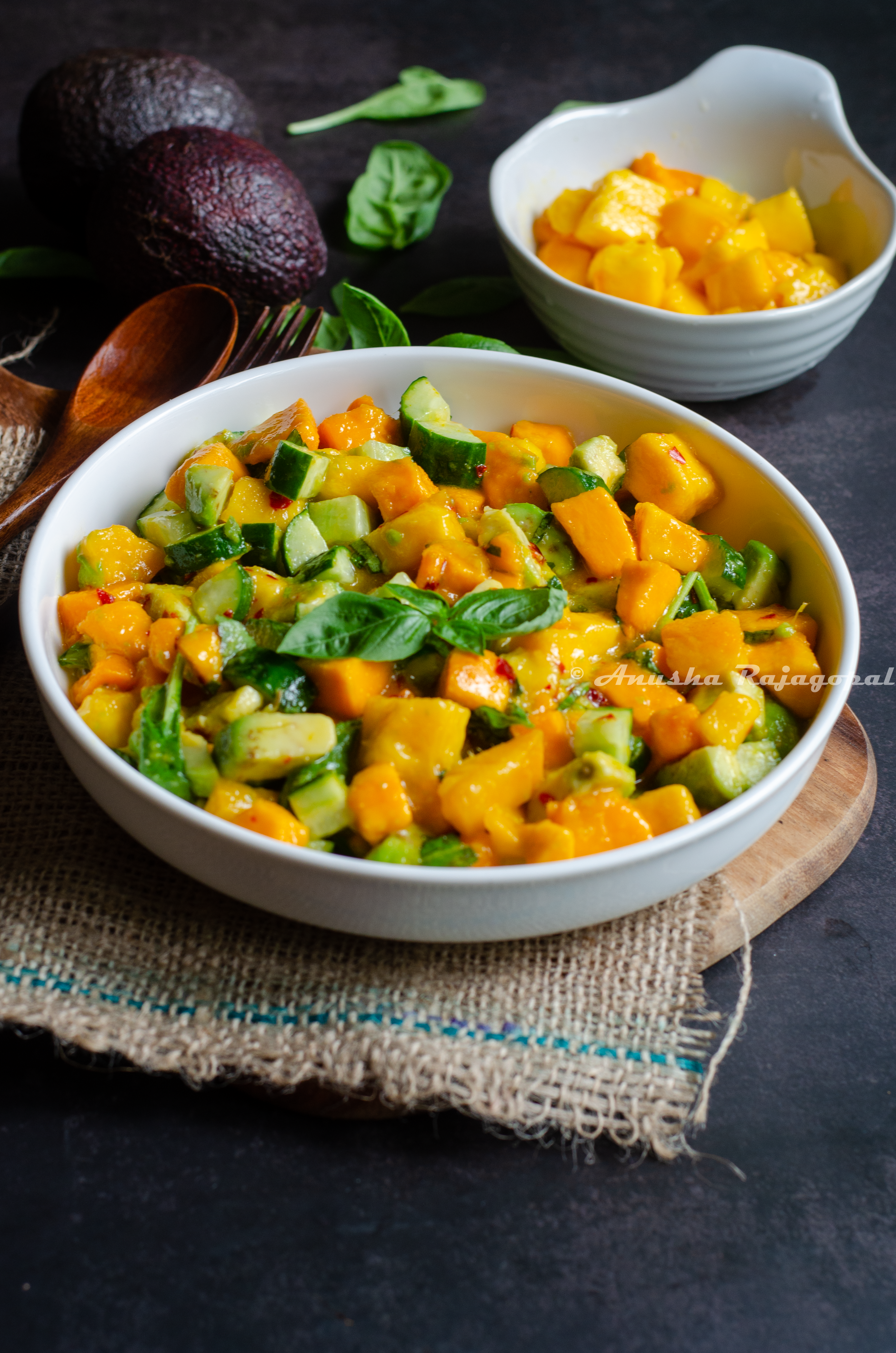 Mango avocado salad served in a white deep plate placed on a burlap mat. Mango cubes in a bowl, herbs and avocado by the sides