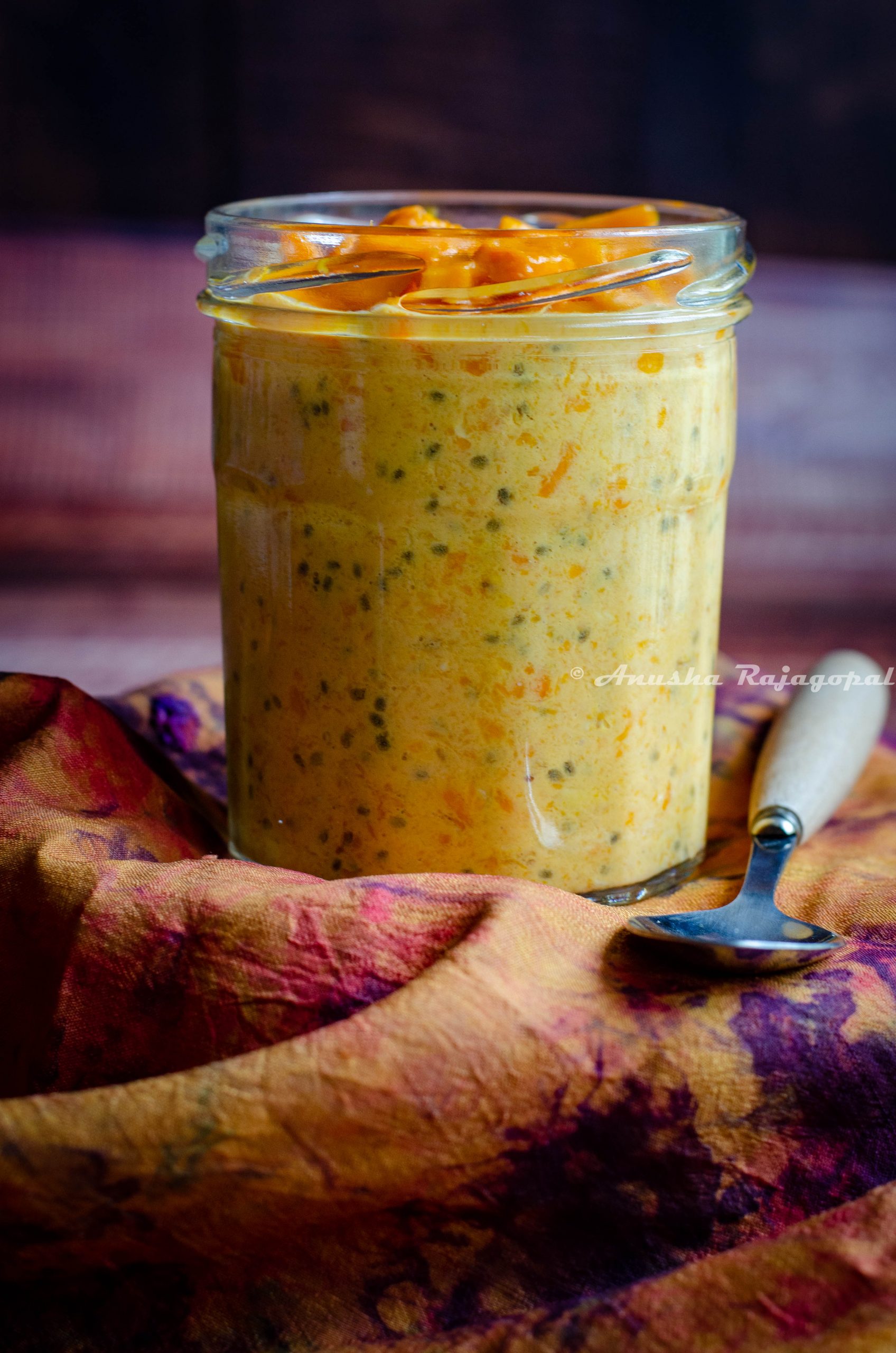 mango coconut overnight oats in a jar placed on a tie-dye towel with a spoon beside.