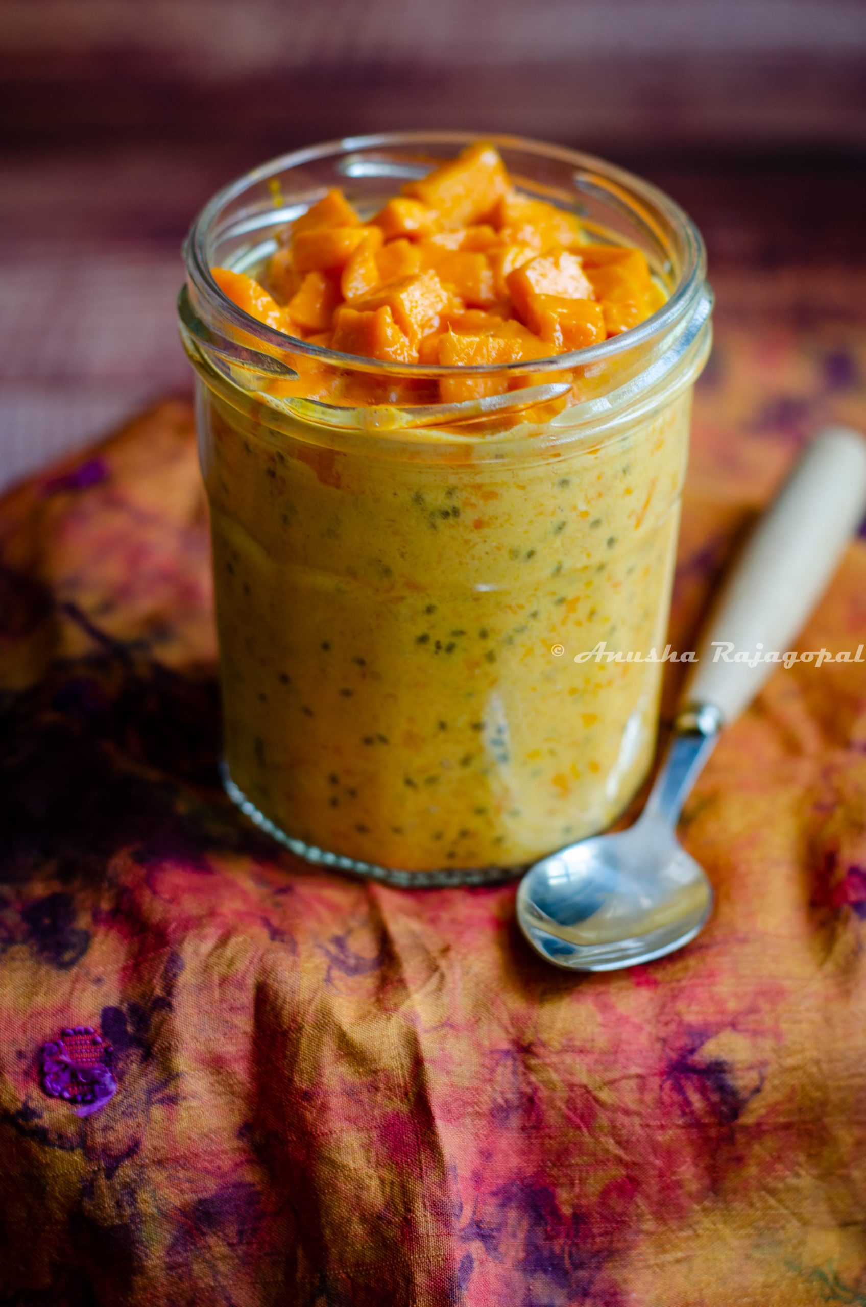 mango coconut overnight oats in a jar placed on a tie-dye towel with a spoon beside.