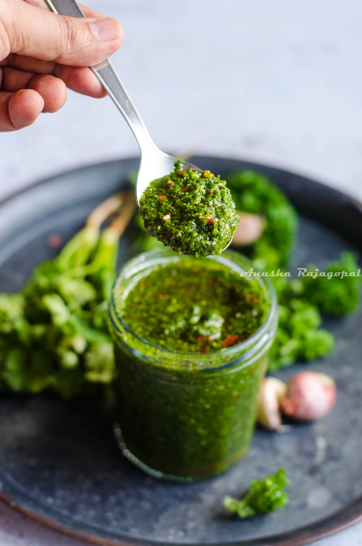 cilantro chimichurri in a glass jar with a spoon of chimichurri held over it.