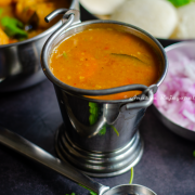 hotel style tiffin sambar served in a pail with idli, vada,chopped onions and a ladle by the side.