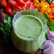 avocado green goddess dressing sauce served in a creamer placed on a chopping board with cut veggies.