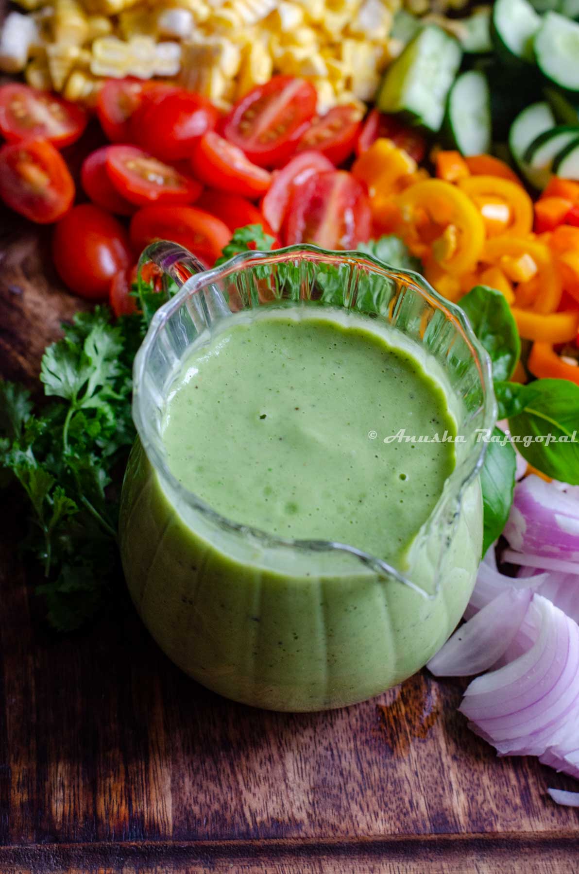 avocado green goddess dressing sauce served in a creamer placed on a chopping board with cut veggies.