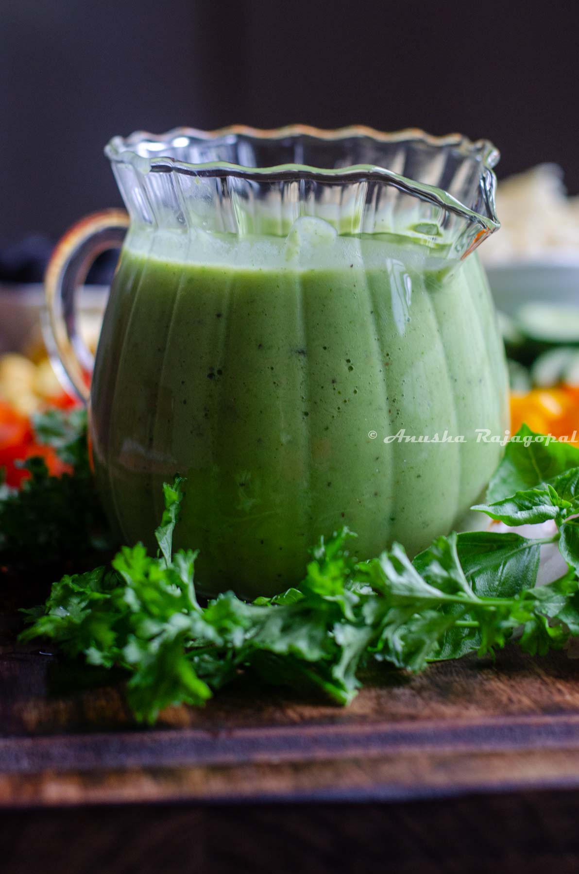 avocado green goddess dressing sauce served in a creamer placed on a chopping board with cut veggies.