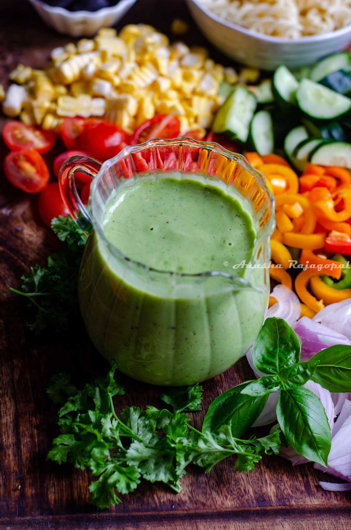 avocado green goddess dressing sauce served in a creamer placed on a chopping board with cut veggies.