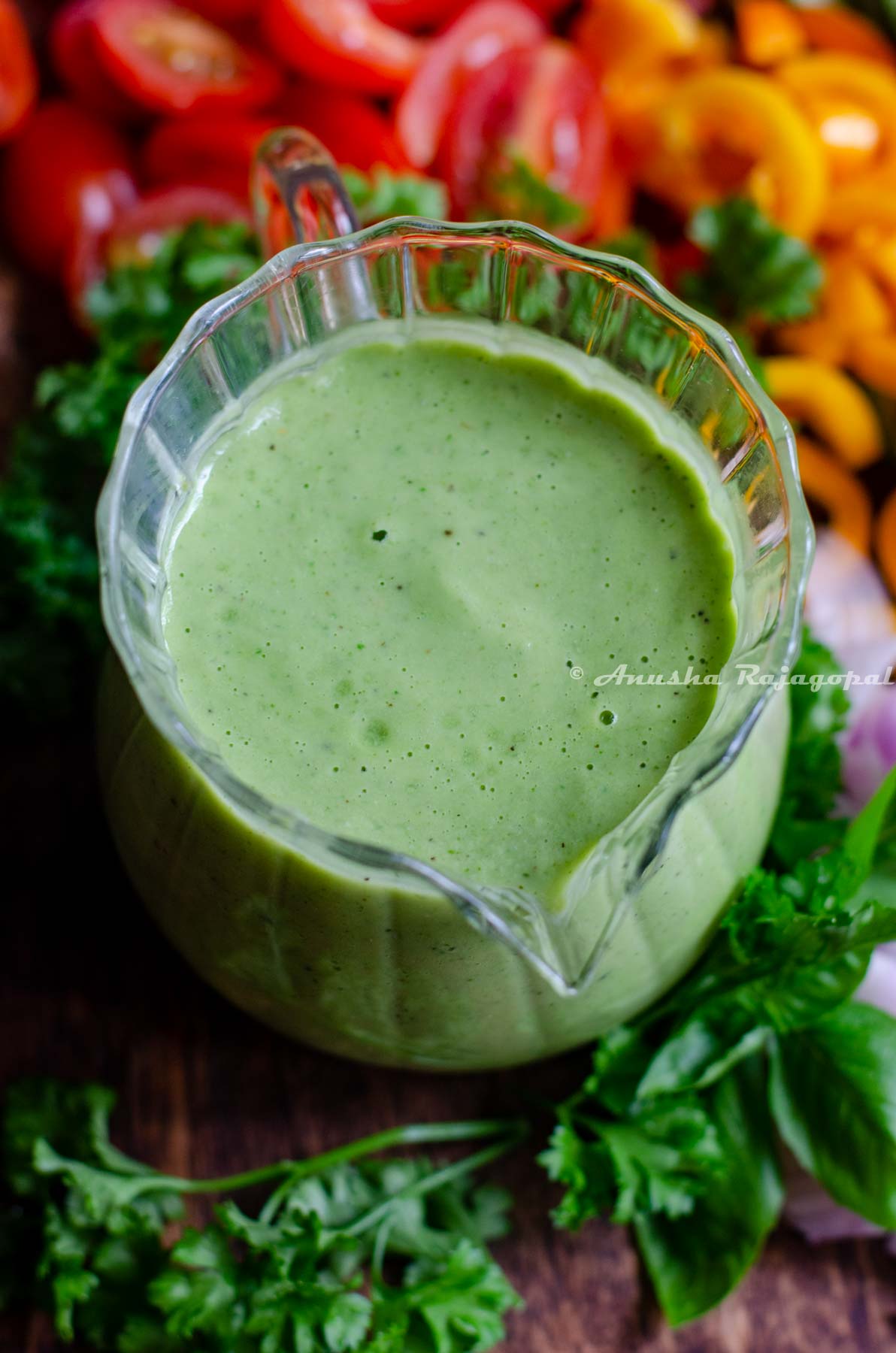 avocado green goddess dressing sauce served in a creamer placed on a chopping board with cut veggies.