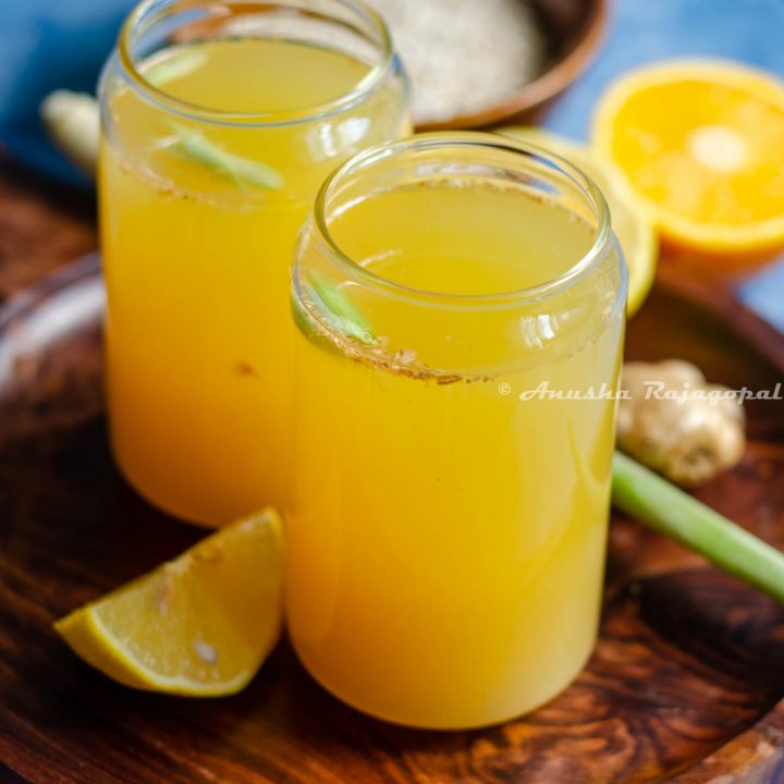 barley lemonade with orange and ginger served in a wooden platter. Lemon wedges, orange halves and lemon grass with a knob of ginger by the side.