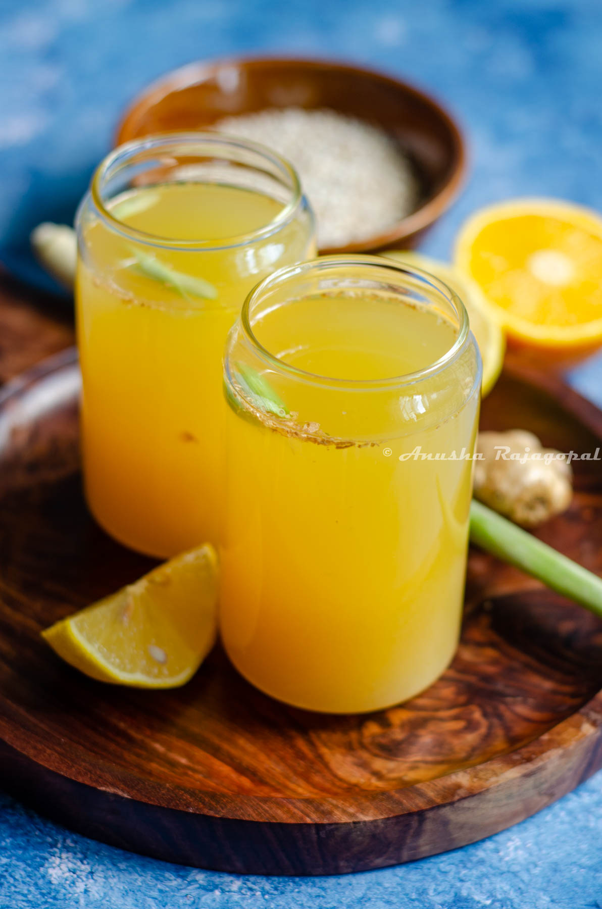 barley lemonade with orange and ginger served in a wooden platter. Lemon wedges, orange halves and lemon grass with a knob of ginger by the side.