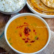 instant pot vegan dahl served in a white bowl placed on a burlap mat. Dahl topped with a garlic and paprika tempering. Jeera rice and Gobi paratha at the background.