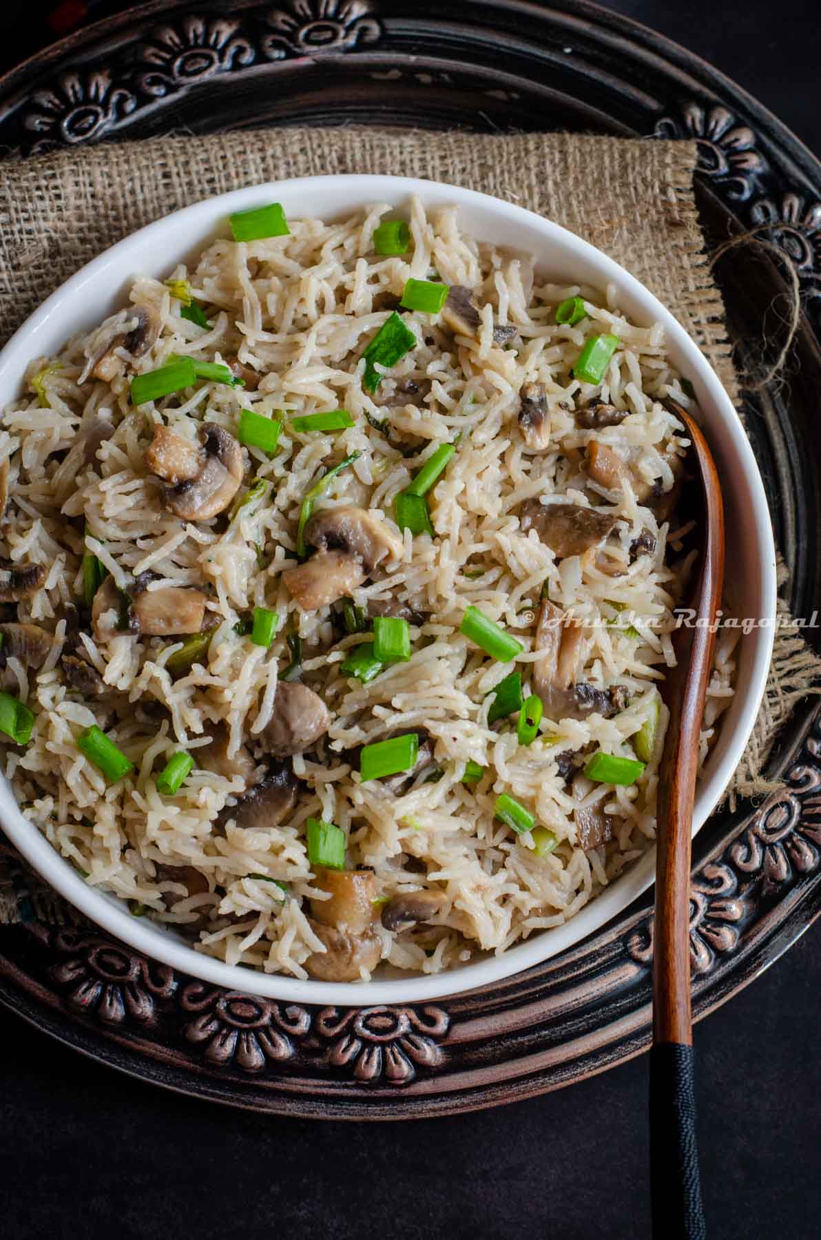 Instant pot mushroom rice served in a white bowl placed over a burlap mat. A spoon has been inserted into the bowl.