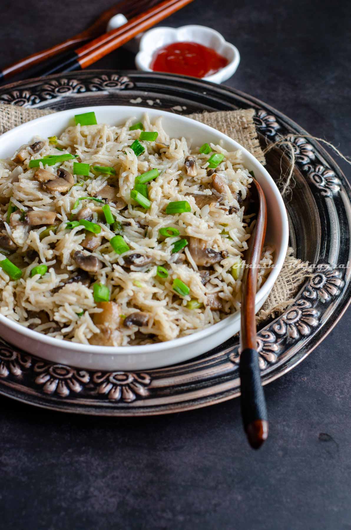 Instant pot mushroom rice served in a white bowl placed over a burlap mat. Ketchup and cutlery by the side.