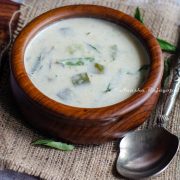 Instant pot zucchini Kootu served in a wooden bowl placed over a burlap mat. A serving spoon by the side. Curry leaves scattered at the back ground.