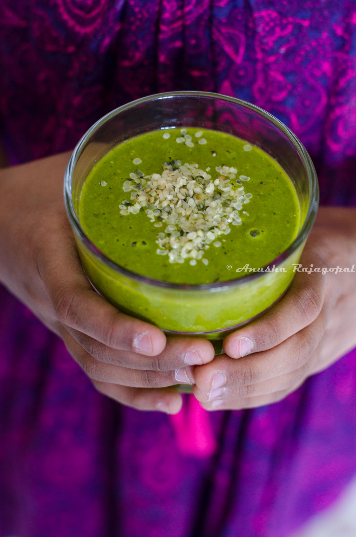 mango spinach smoothie held in hands. Hemp seeds topped over the smoothie.