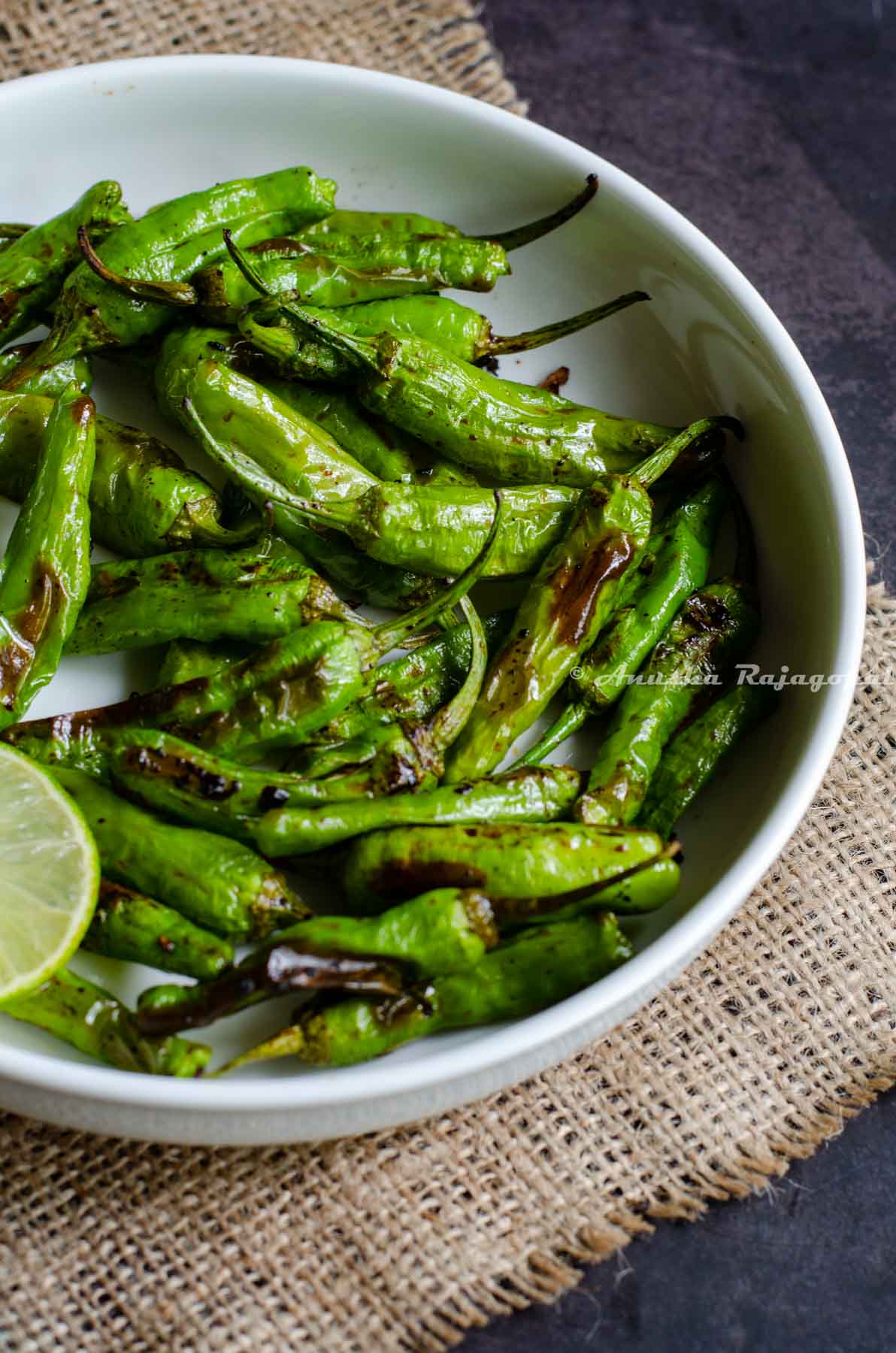 Shishito peppers charred in air fryer and served in a white platter with lime wedges by the side.