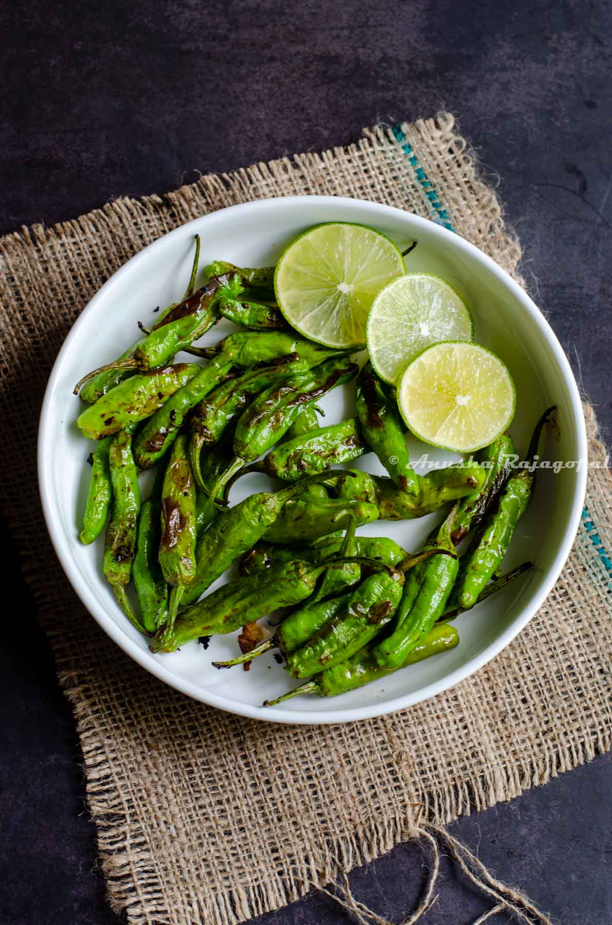 Shishito peppers charred in air fryer and served in a white platter with lime wedges by the side.