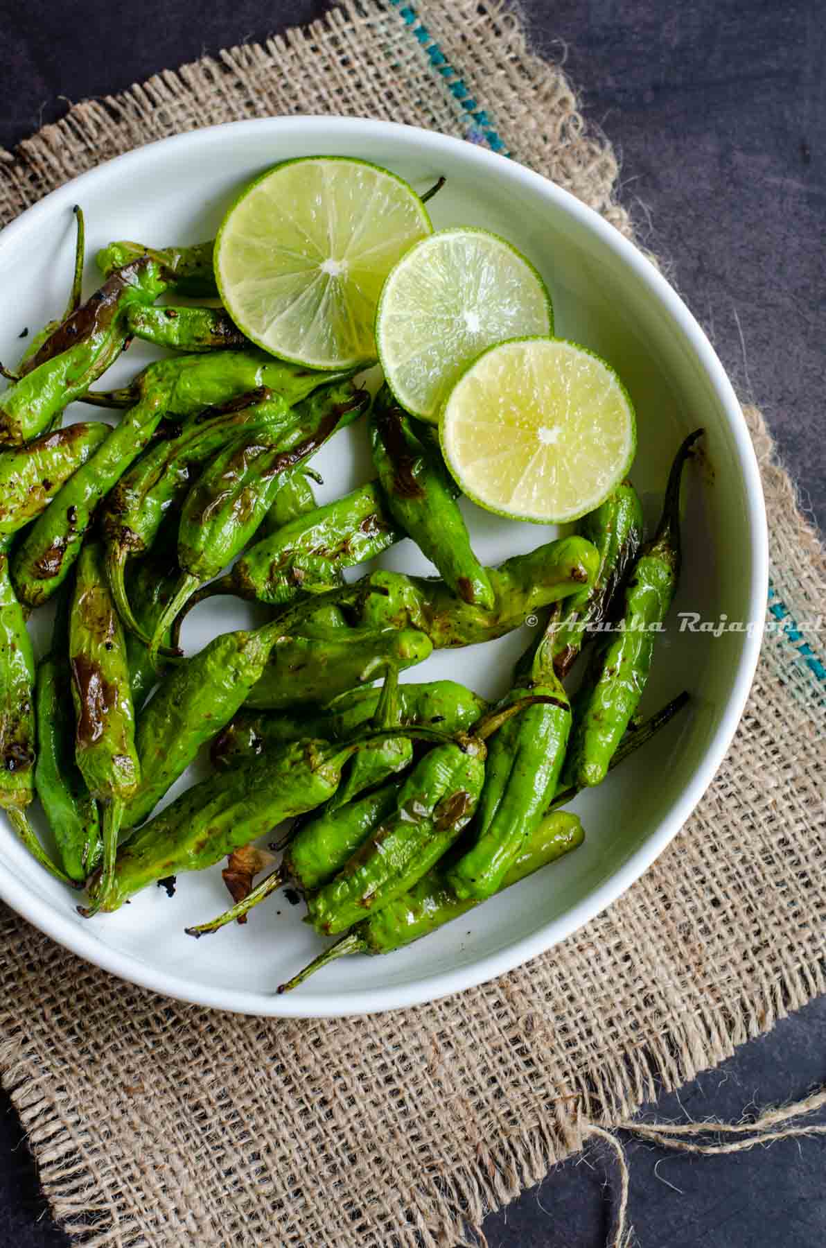 Shishito peppers charred in air fryer and served in a white platter with lime wedges by the side.