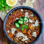 butternut squash chili served in a black bowl topped with jalapenos, tortilla chips and cilantro.