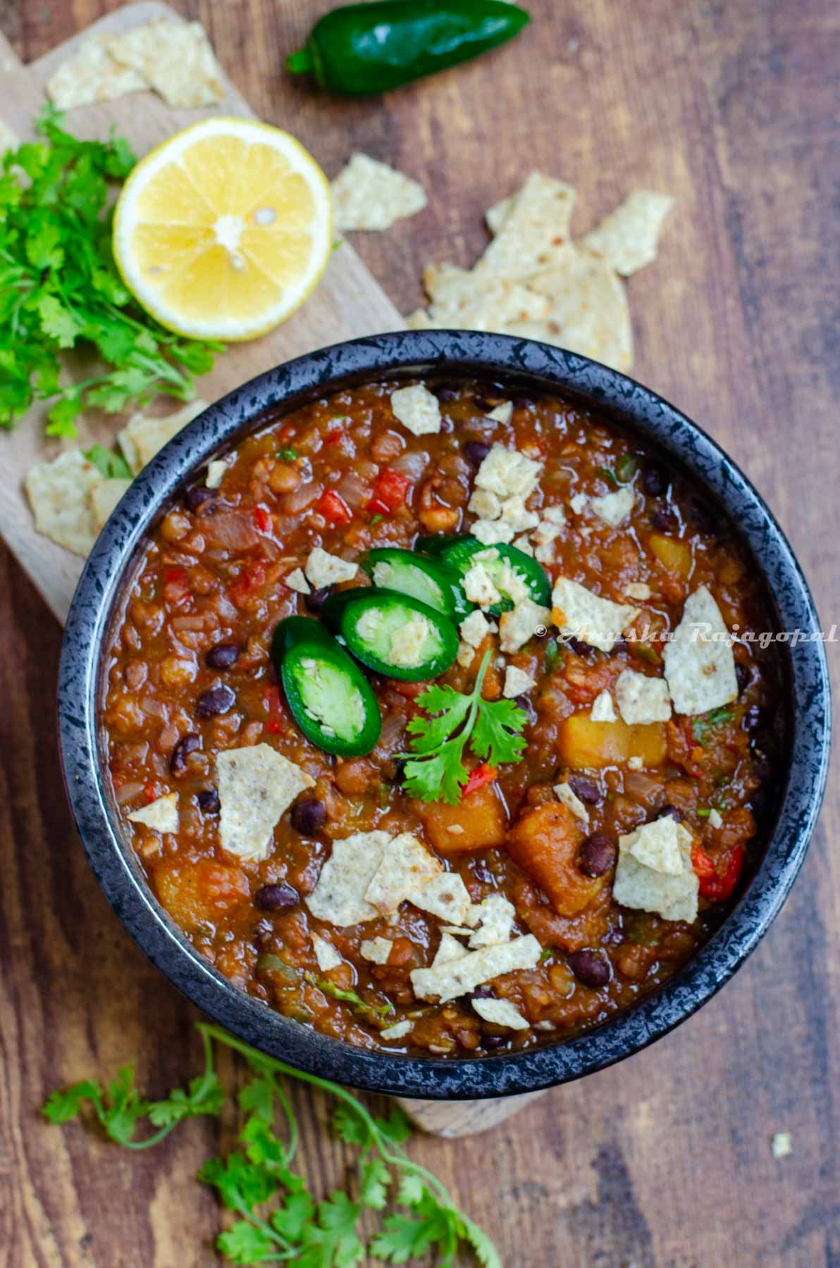 butternut squash chili served in a black bowl topped with jalapenos, tortilla chips and cilantro.