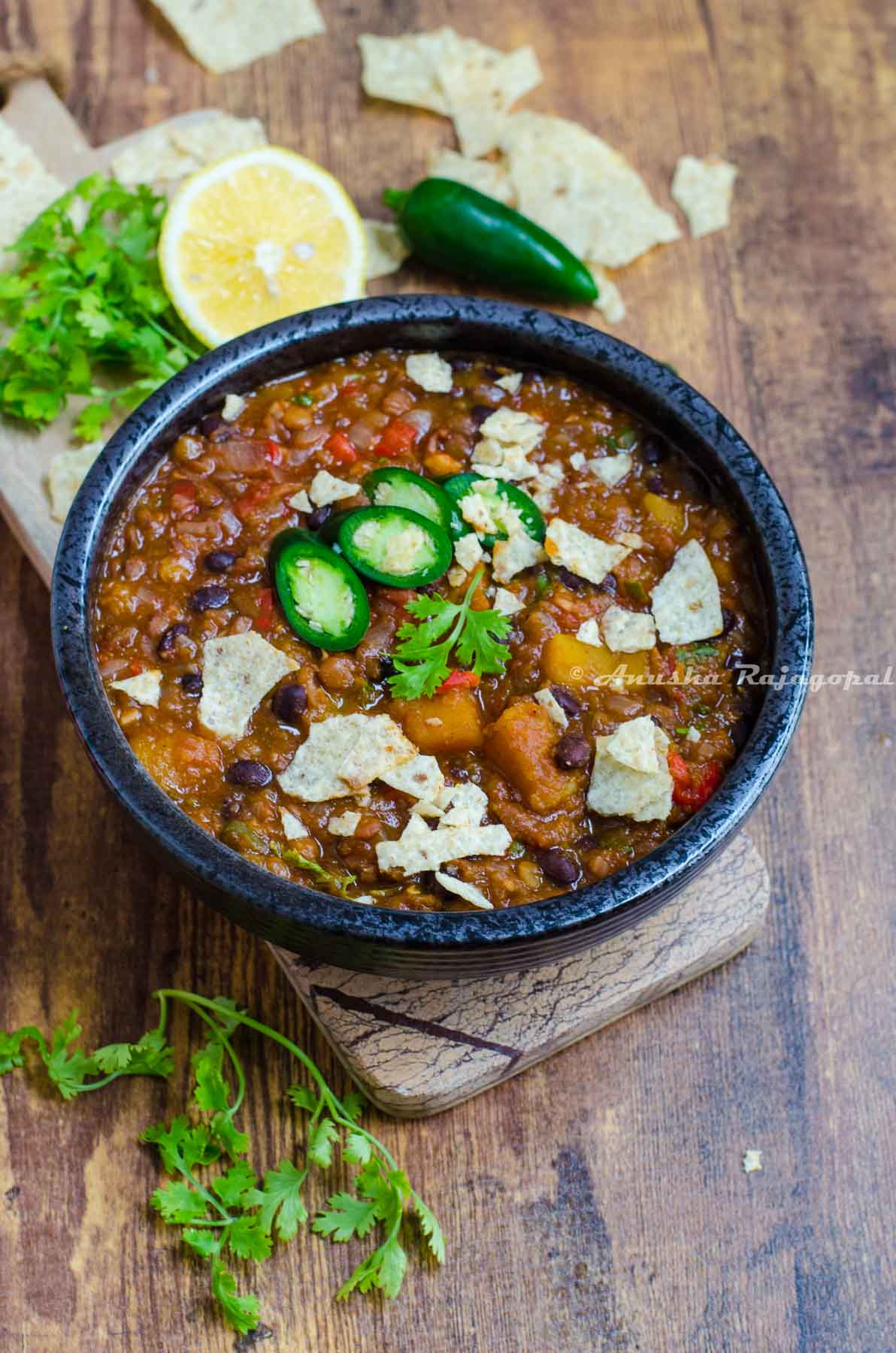 Butternut lentil chili served in a black bowl placed on a cheese board against a wooden table top