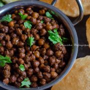 Kala chana made in Instant pot served in a steel pan with pooris placed on a black platter