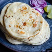 vegan naans stacked on a metal plate and served with onions and lemon wedges