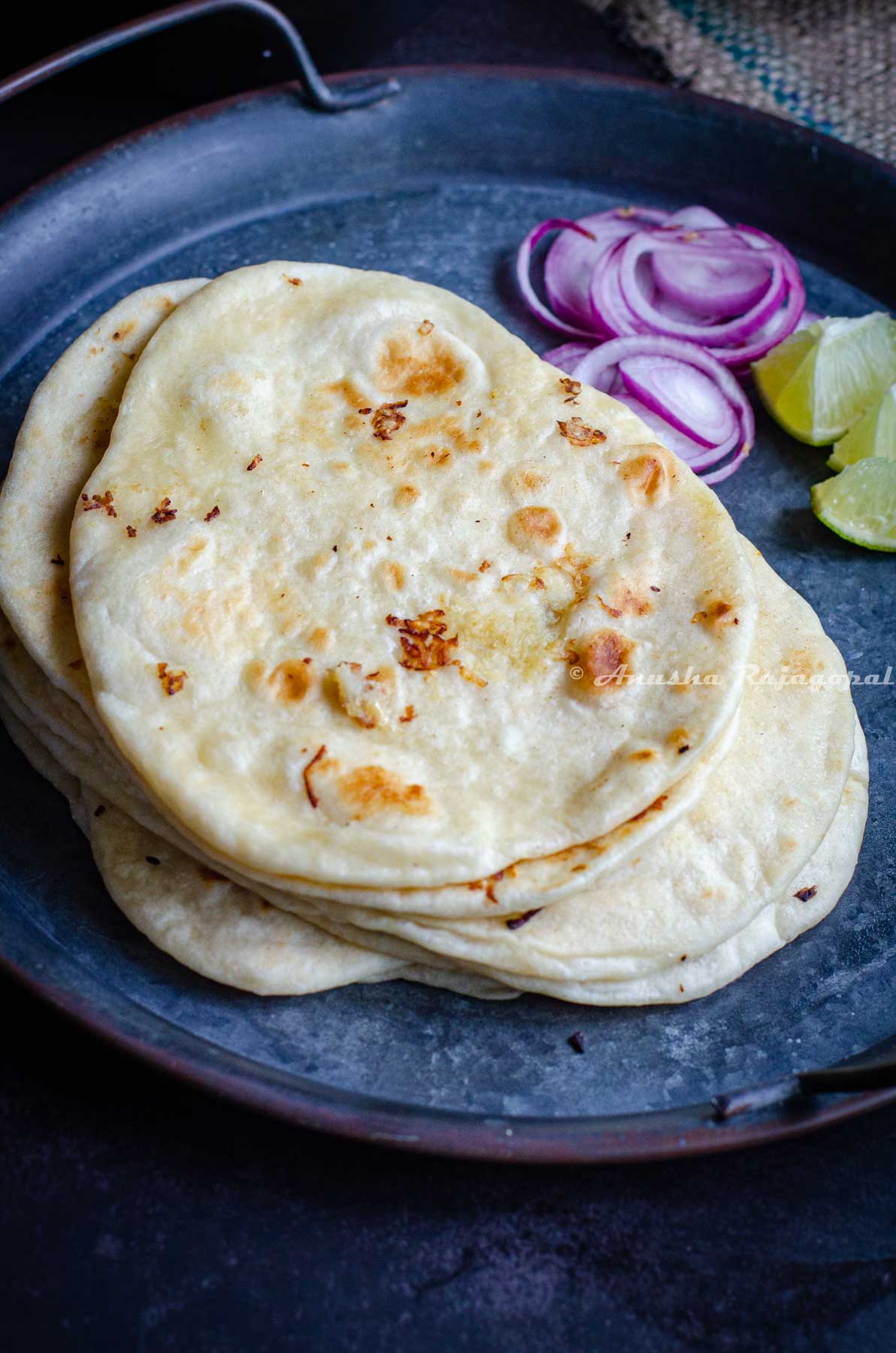 vegan naans stacked on a metal plate and served with onions and lemon wedges