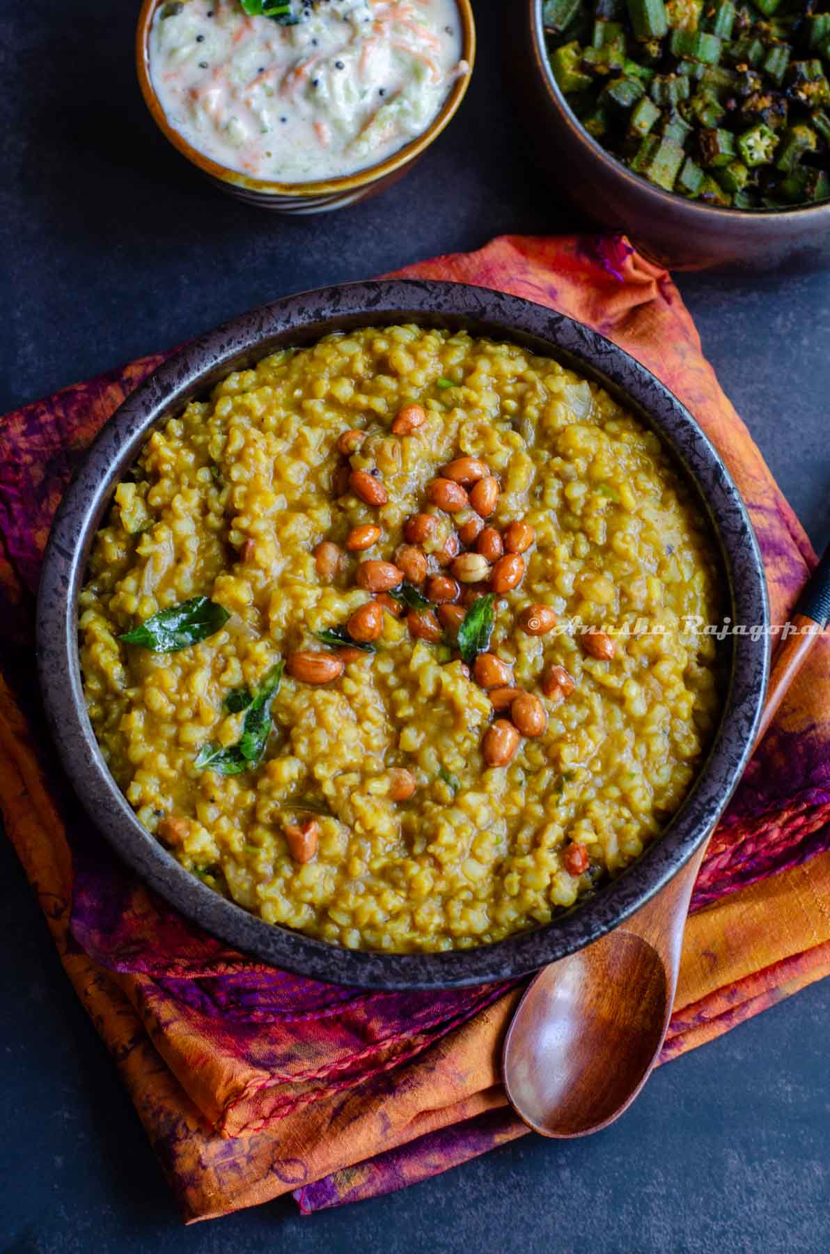 Instant pot sambar rice served in a black bowl topped with roasted peanuts. The bowl is placed over a tye-dye patterned napkin. A spoon is also by the side of the bowl.