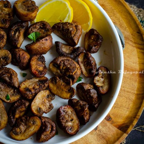 air fryer mushrooms served on a deep white plate with lemon wedges. White plate placed on a wooden plate.