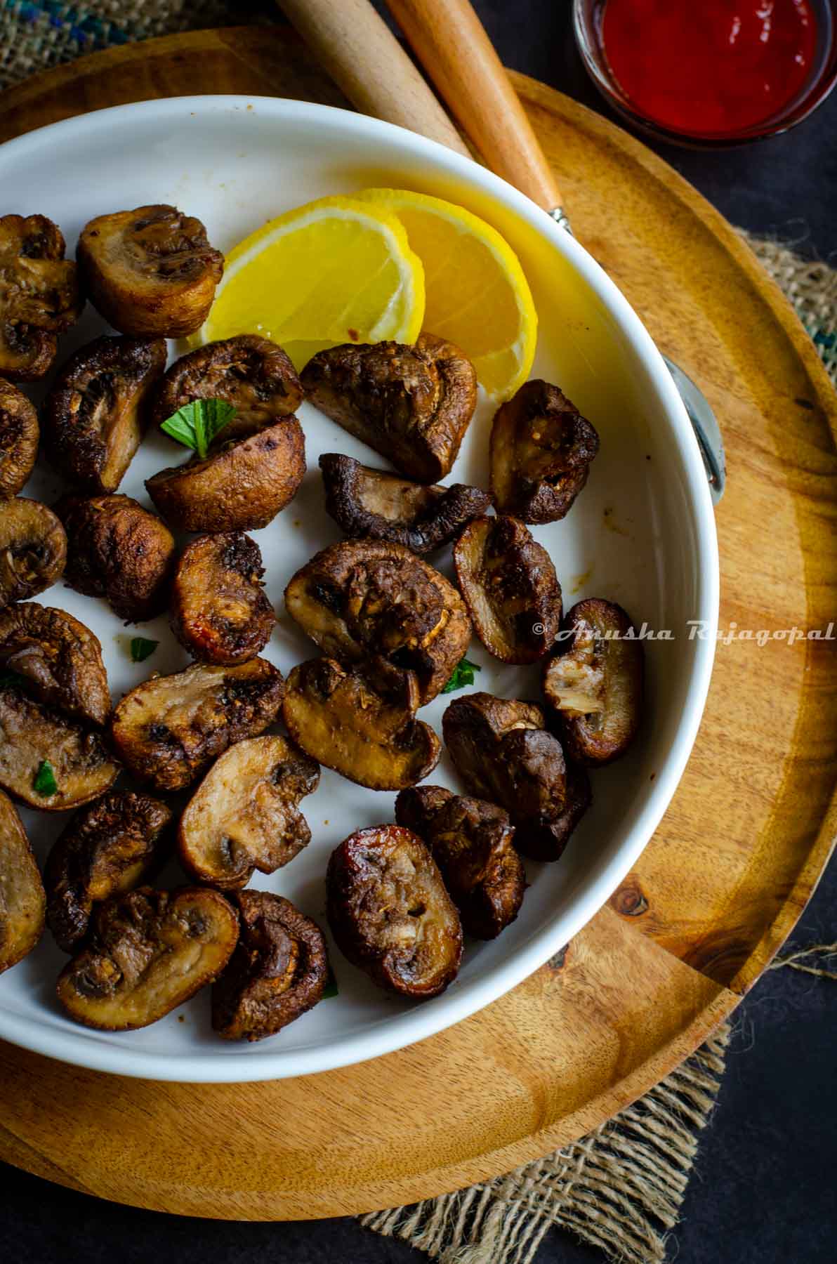 air fryer mushrooms served on a deep white plate with lemon wedges. White plate placed on a wooden plate.