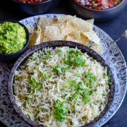 Mexican style cilantro lime rice served in a black dish with guacamole, tortilla chips and other condiments at the background.