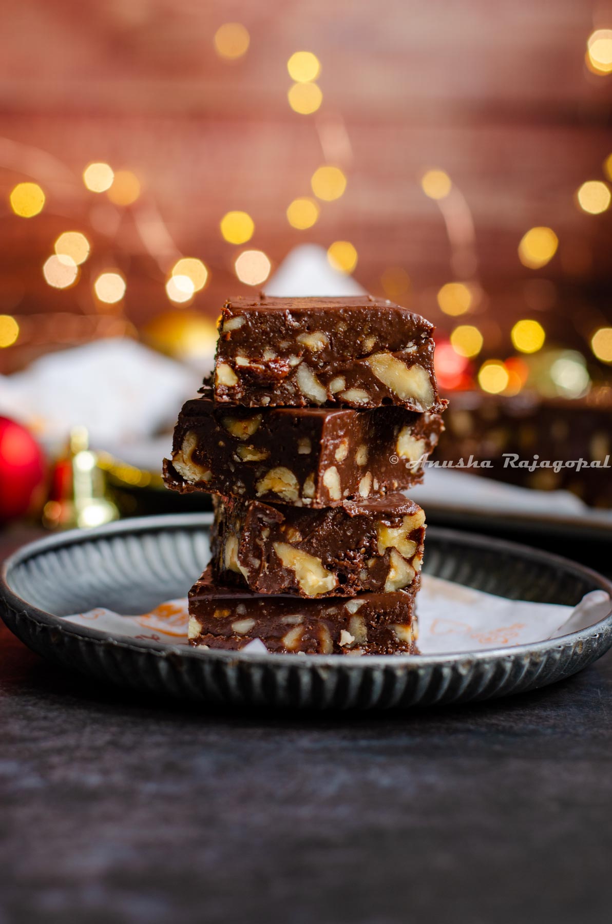 Instant pot fudge stacked over a piece of parchment paper placed on a rustic metal tray. Christmas ornaments placed at the back. Fairy lights not in focus.