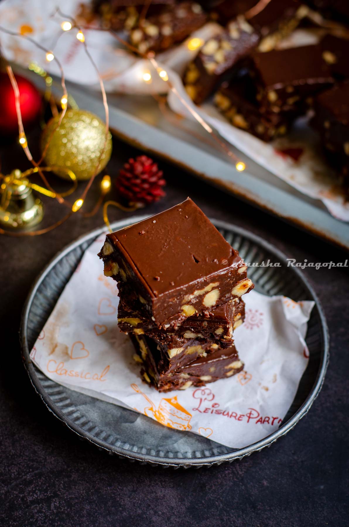 Instant Pot fudge stacked over a piece of parchment paper placed on a rustic metal tray. Christmas ornaments placed at the back. Fairy lights not in focus.