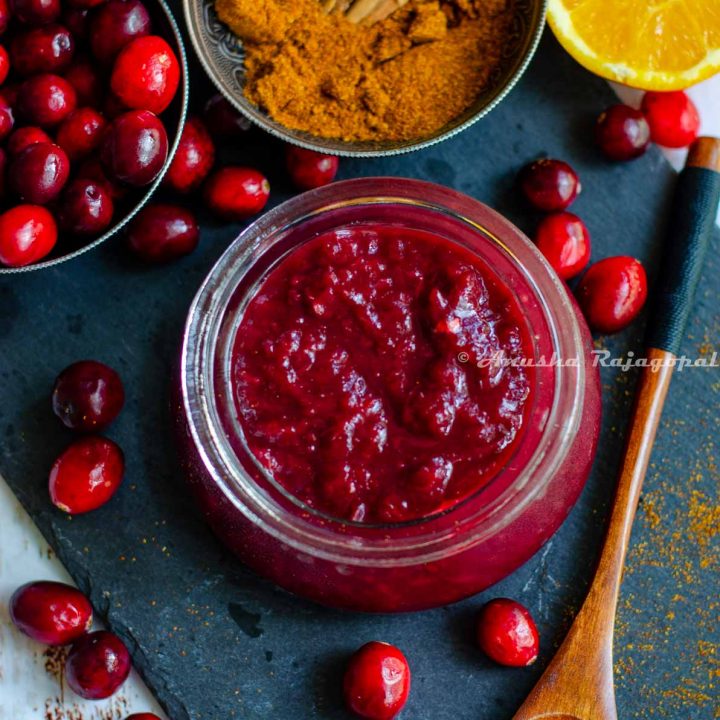 cranberry chutney made in the instant pot, served in a glass jar placed over a slate board. Cranberries, halved oranges and spices by the side.
